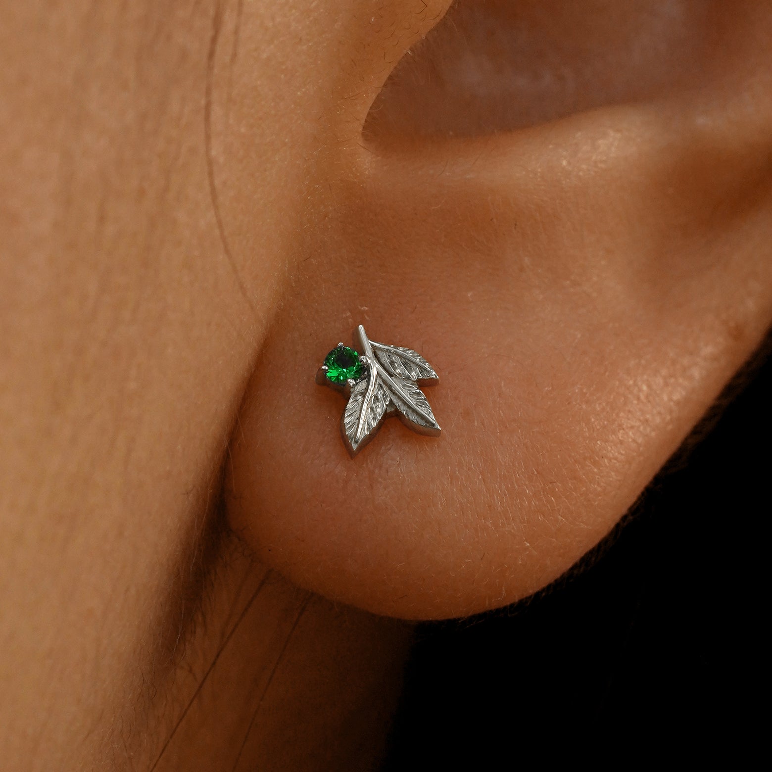 Close up view of a model's ear wearing a 14k white gold emerald 3 Leaves Gemstone Earring
