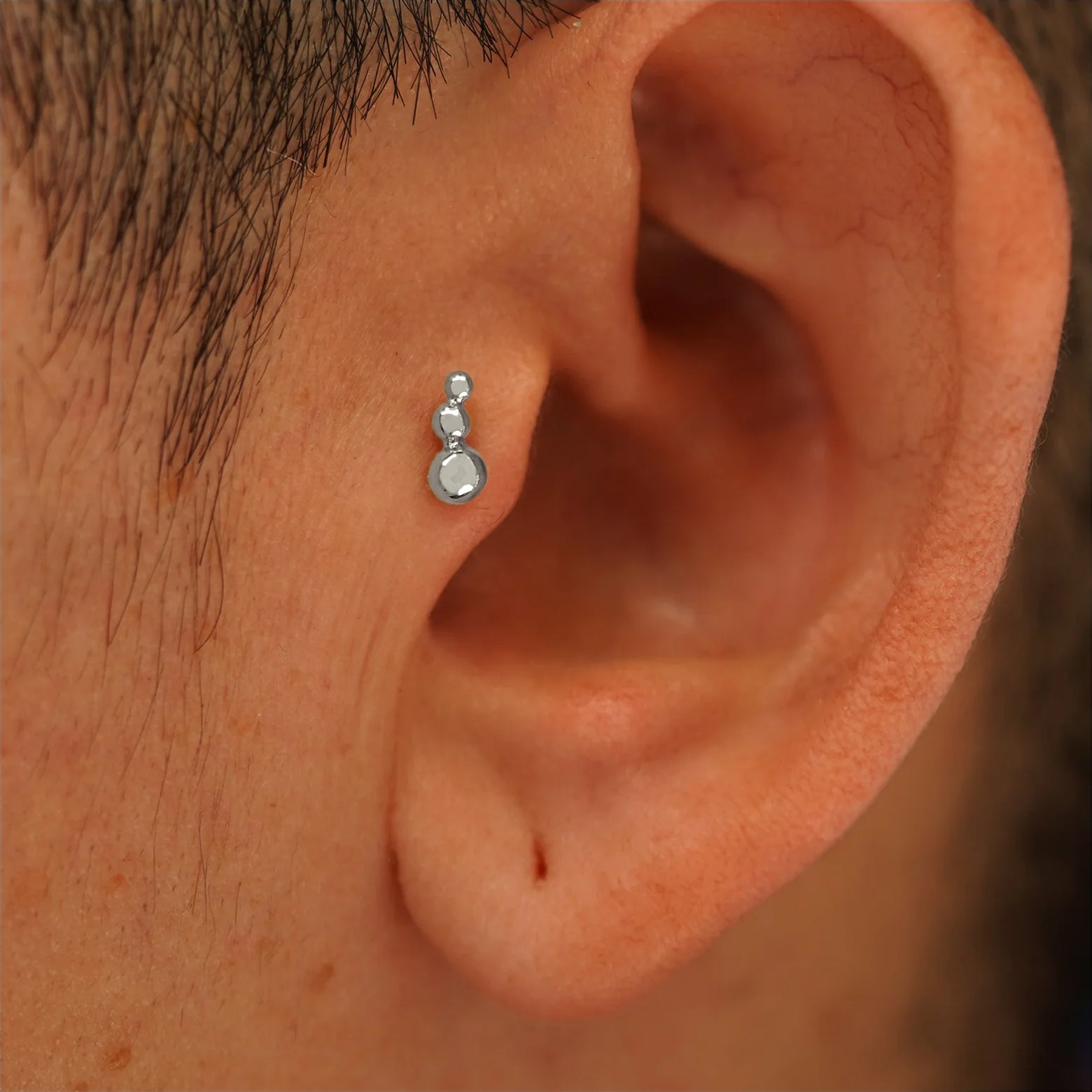 Close up view of a model's ear wearing a 14k gold gold Graduated Ball Flatback as a tragus piercing