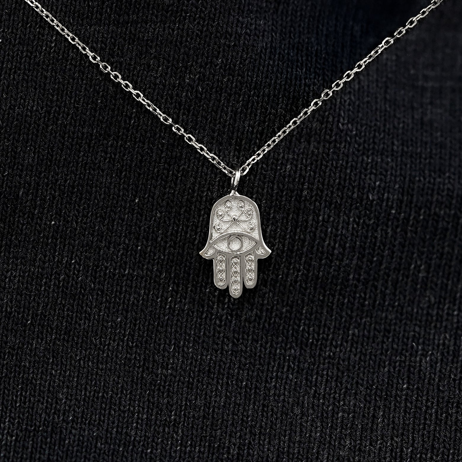 Close up view of a solid 14k white gold hamsa necklace against a model's black shirt