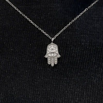 Close up view of a solid 14k white gold hamsa necklace against a model's black shirt
