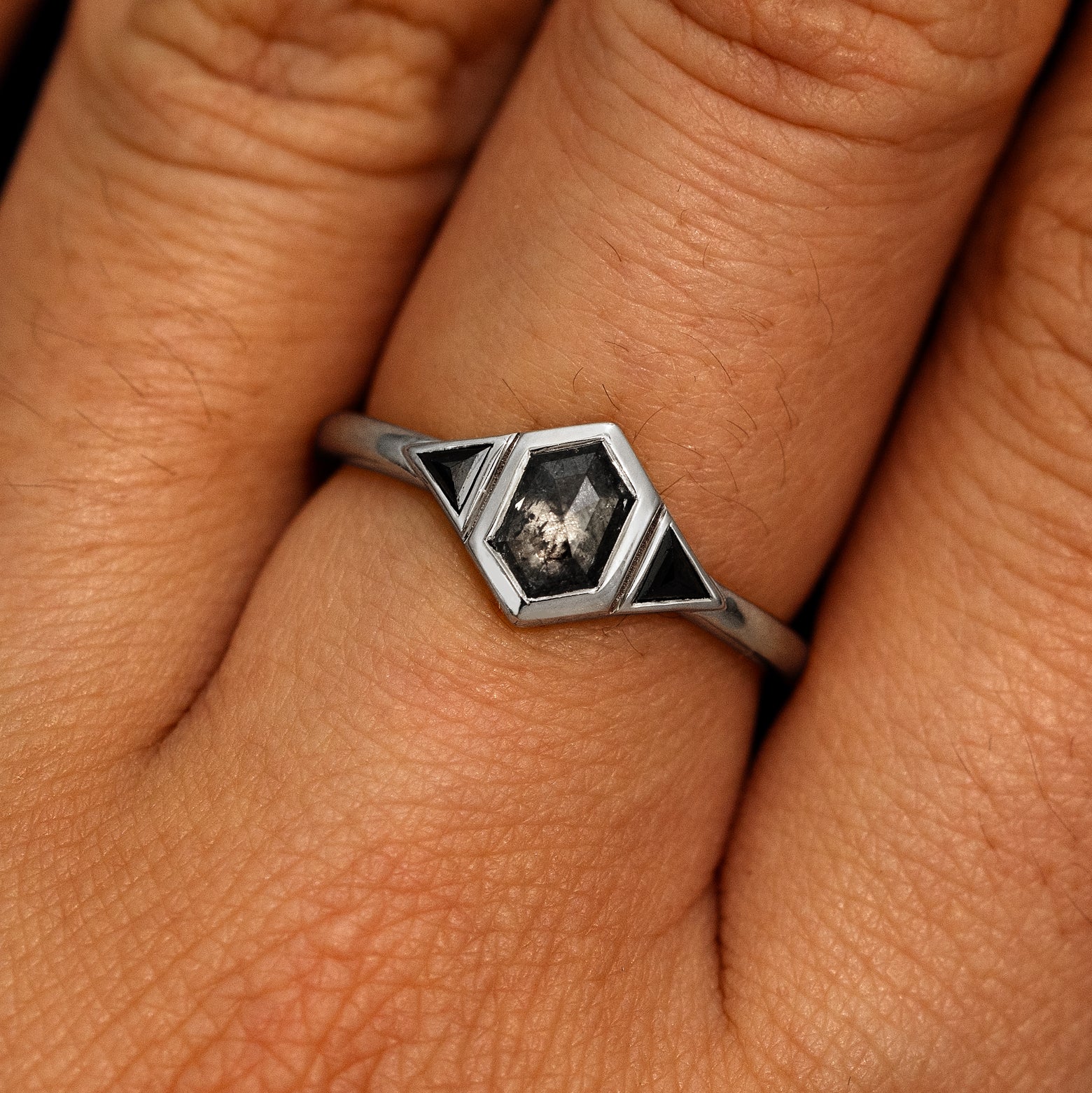 A model's hand wearing a 14k white gold Hexagon Salt and Pepper and Triangle Black Diamond Three Stone Ring