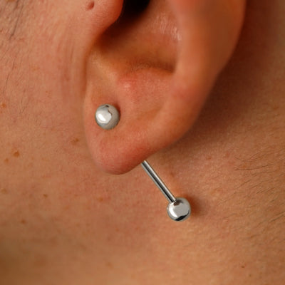 Close up view of a model's ear wearing a 14k white gold Large Straight Barbell through a lobe piercing