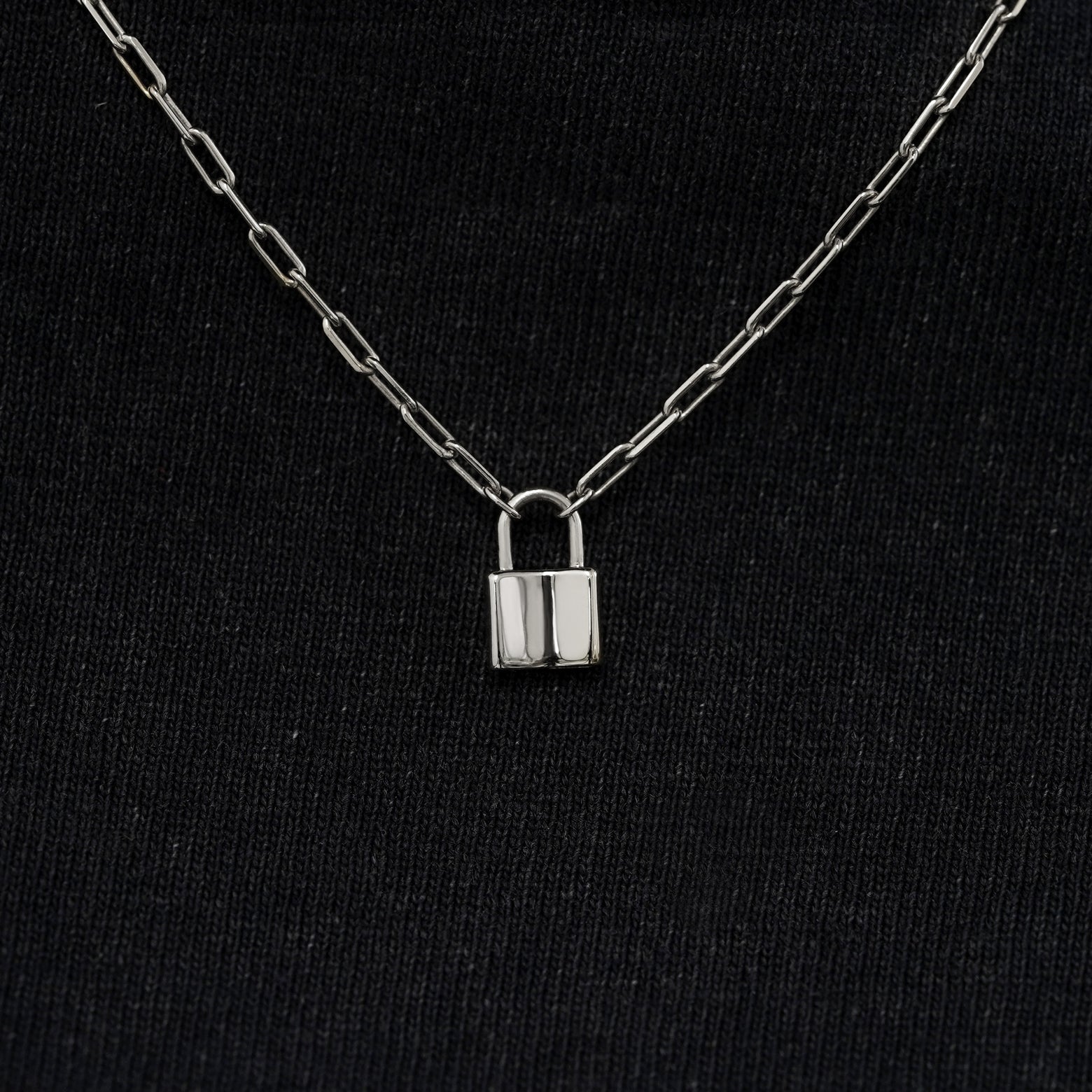 Close up view of a solid 14k white gold lock necklace against a model's black shirt