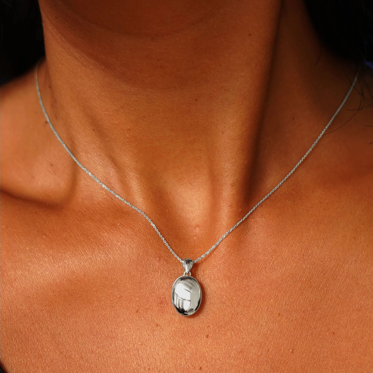 Close up view of a model's neck wearing a white gold Oval Locket Pendant on a Cable Chain