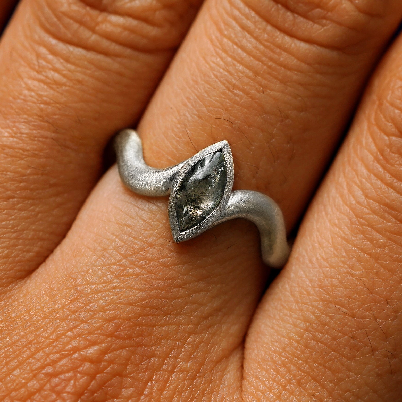 Close up view of a model's hand wearing a 14k white gold marquise cabochon salt and pepper diamond engagement ring