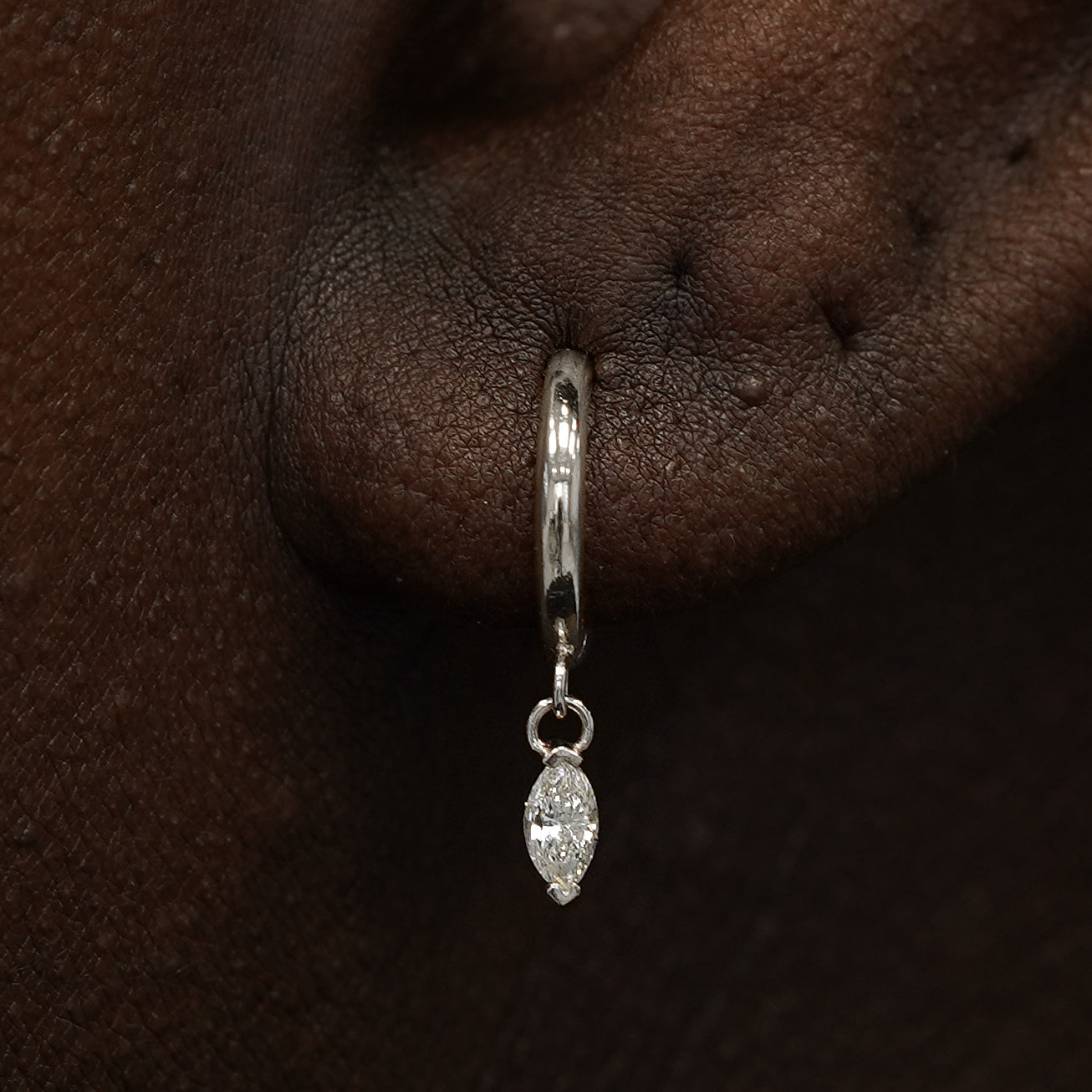 Close up view of a model's ear wearing a white gold Marquise Lab Diamond Dangle Huggie Hoop