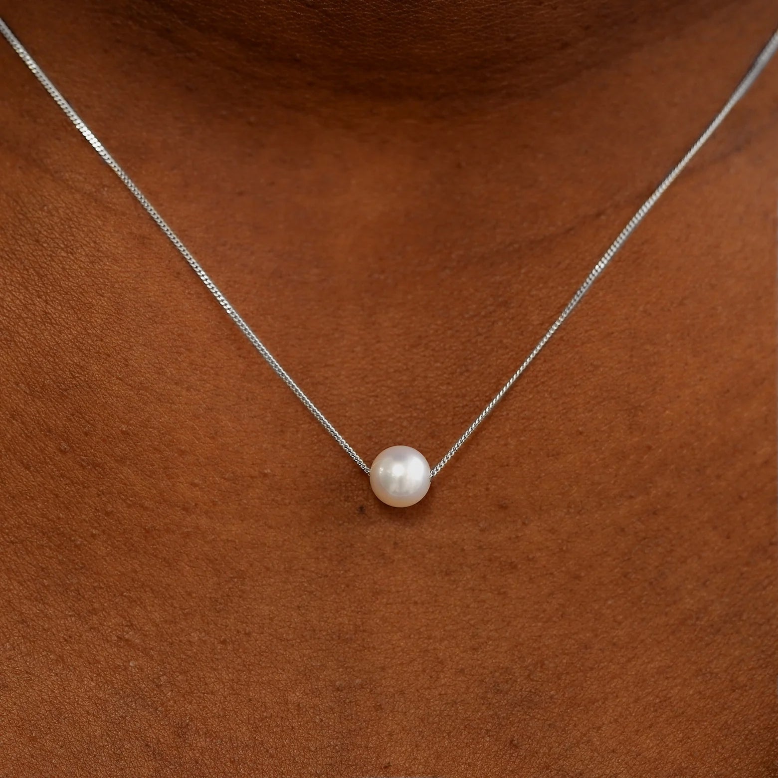 Close up view of a model's neck wearing a white gold Pearl Slide Necklace with a 6mm pearl