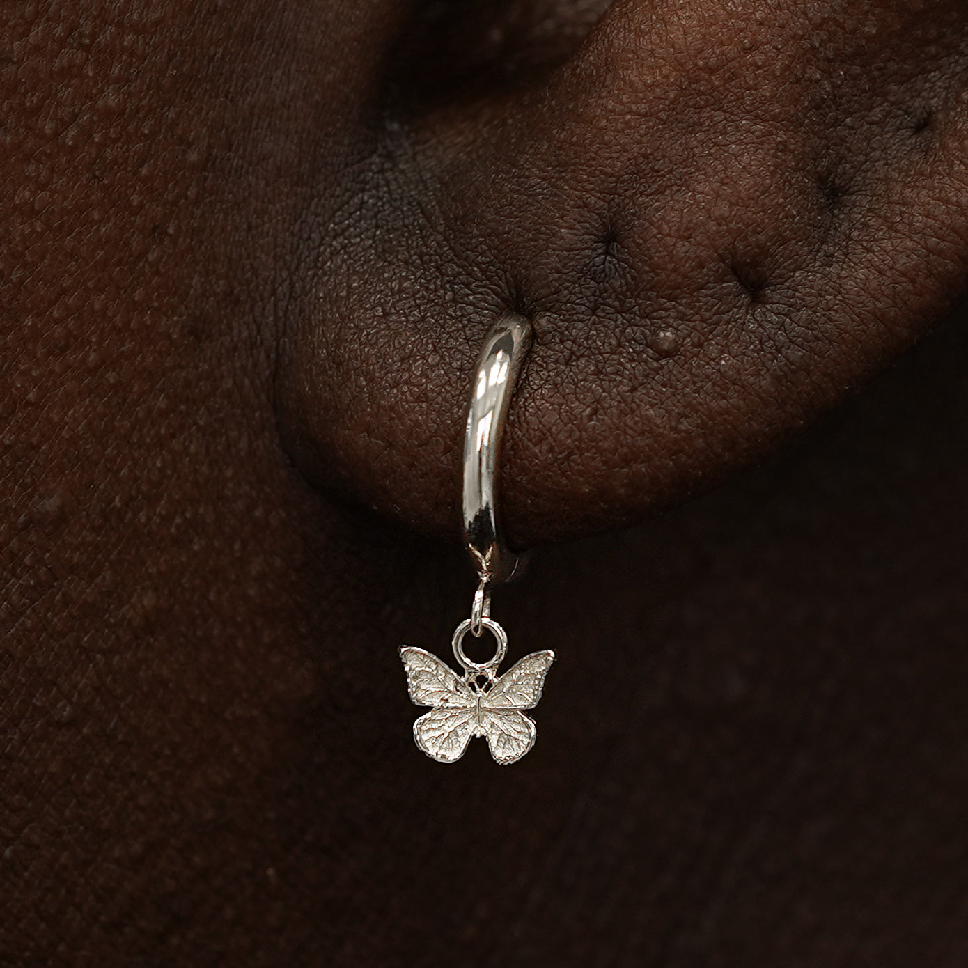 Close up view of a model's ear wearing a white gold Mini Butterfly Dangle Huggie Hoop