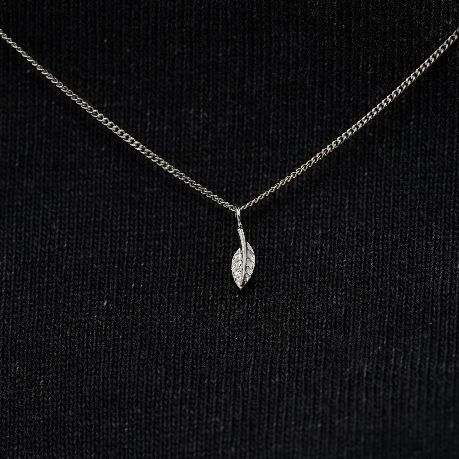Close up view of a solid 14k white gold mini leaf necklace against a model's black shirt