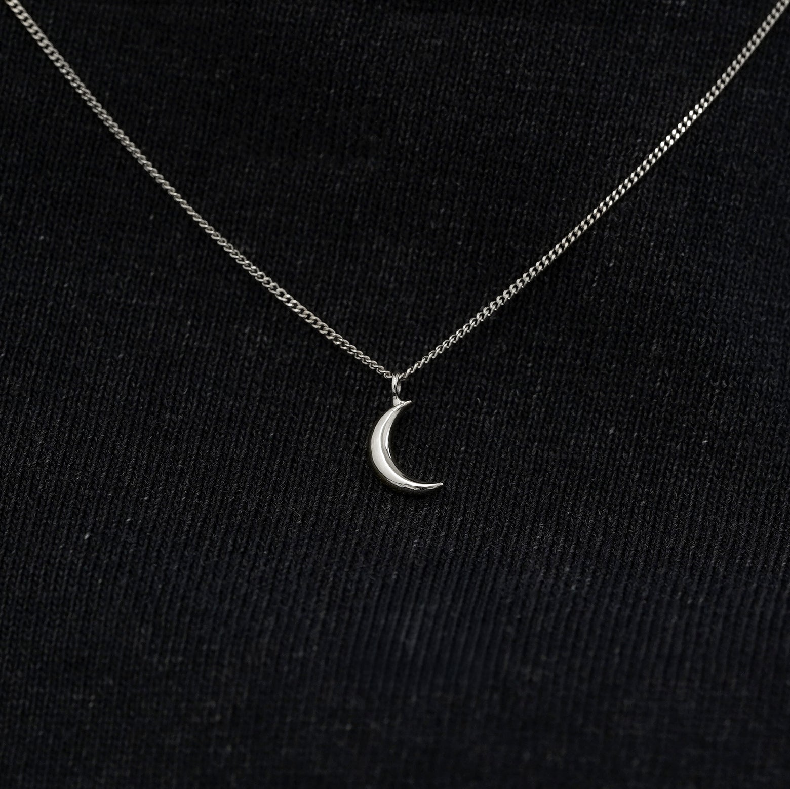 Close up view of a solid 14k white gold moon necklace against a model's black shirt