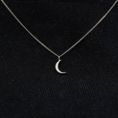 Close up view of a solid 14k white gold moon necklace against a model's black shirt