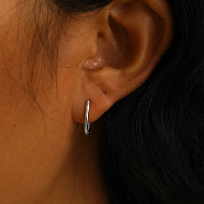 A model's ear wearing a 14 karat white gold Oval Huggie Hoop