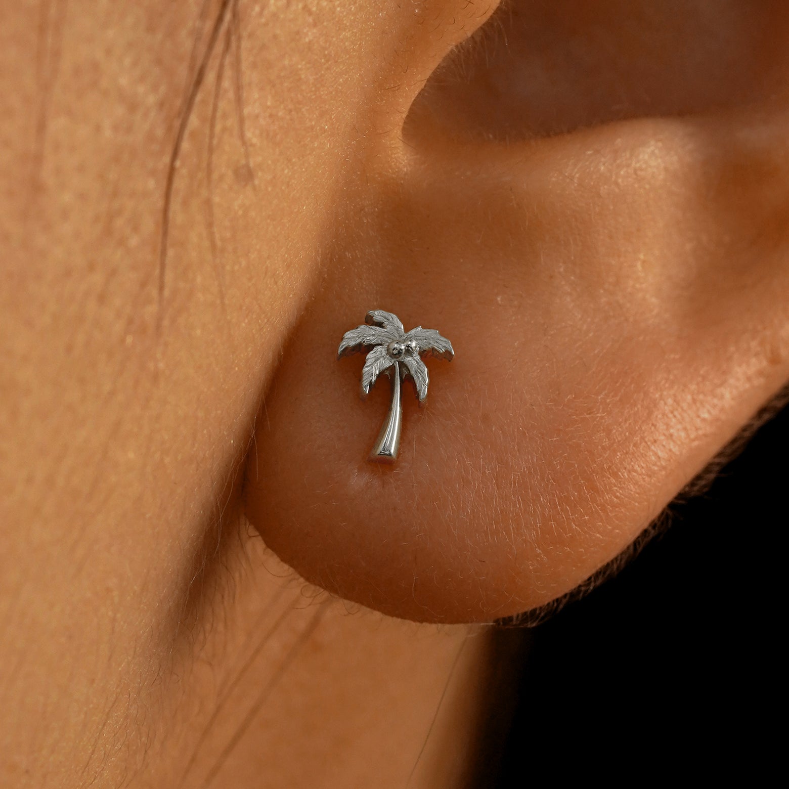 Close up view of a model's ear wearing a 14k white gold Palm Tree Earring