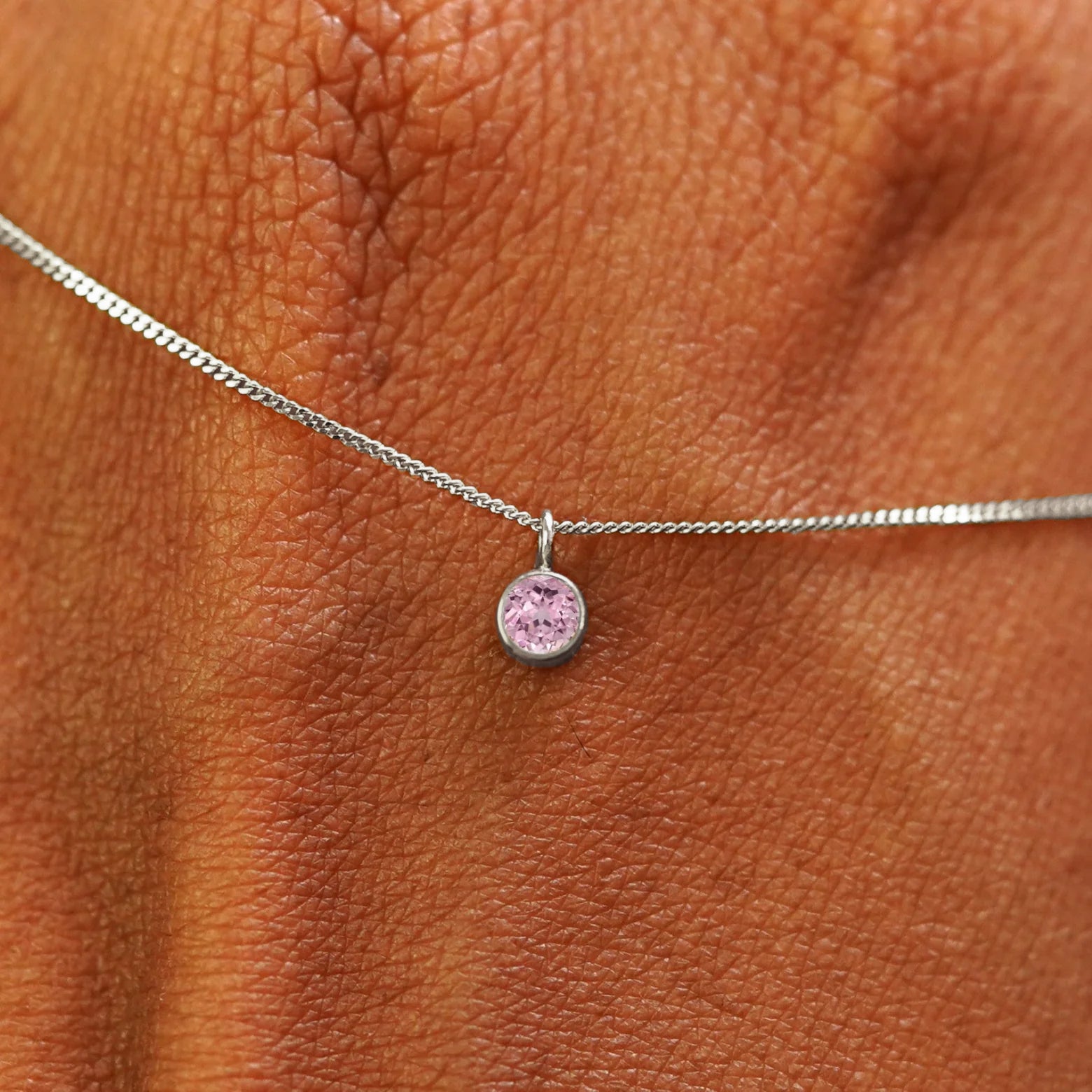 Close up view of a 14k white gold Pink Sapphire Necklace draped across the back of a model's hand