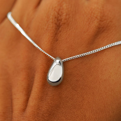 A model's holding a white gold Puffy Teardrop Necklace across the back of their hand