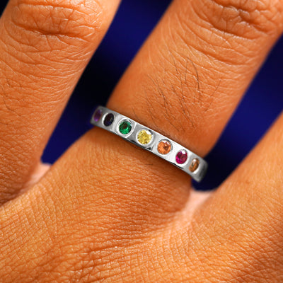 A white gold ring with an emerald, ruby, champagne and black diamonds, and sapphires of multiple colors in rainbow order