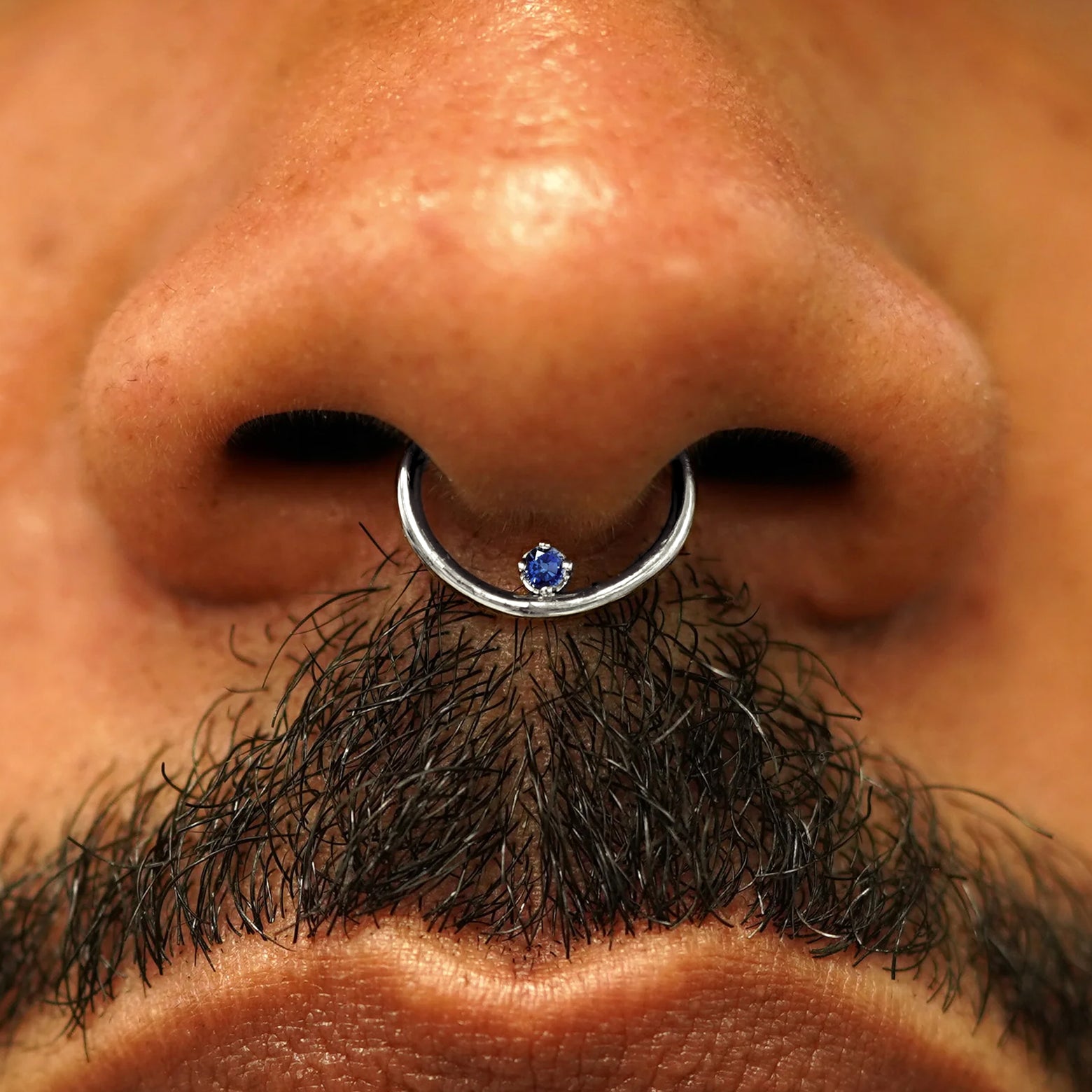 Close up view of a model's nose wearing a 14k white gold sapphire Raised Gemstone Septum