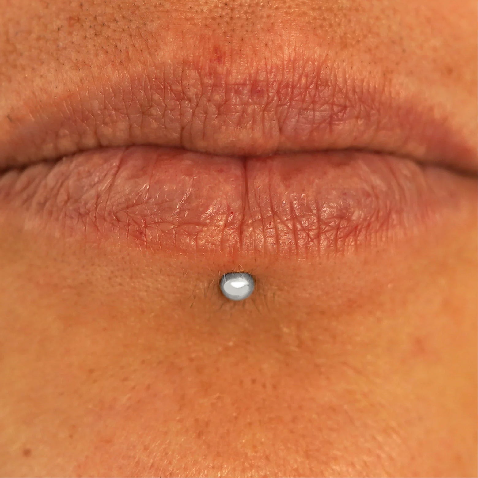 Close up view of a model's lips wearing a 14k white gold Small Labret Piercing