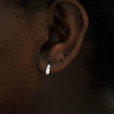 Close up view of a model's ear wearing a 14k white gold Small Wide Huggie Hoop Earring