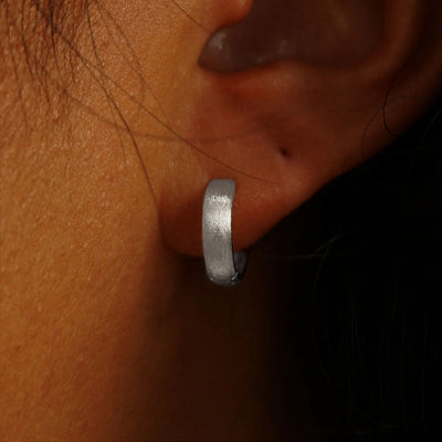 Close up view of a model's ear wearing a 14k white gold Stardust Small Wide Huggie Hoops