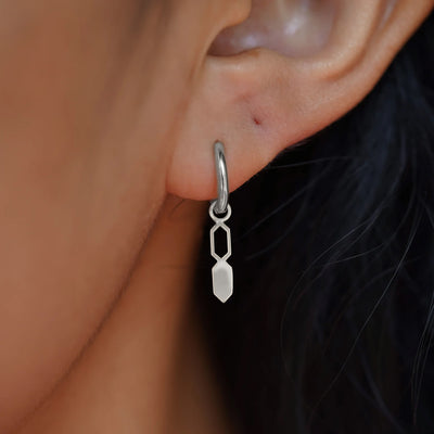 Close up view of a model's ear wearing a white gold Tanlah Charm on a Curvy Huggie Hoop