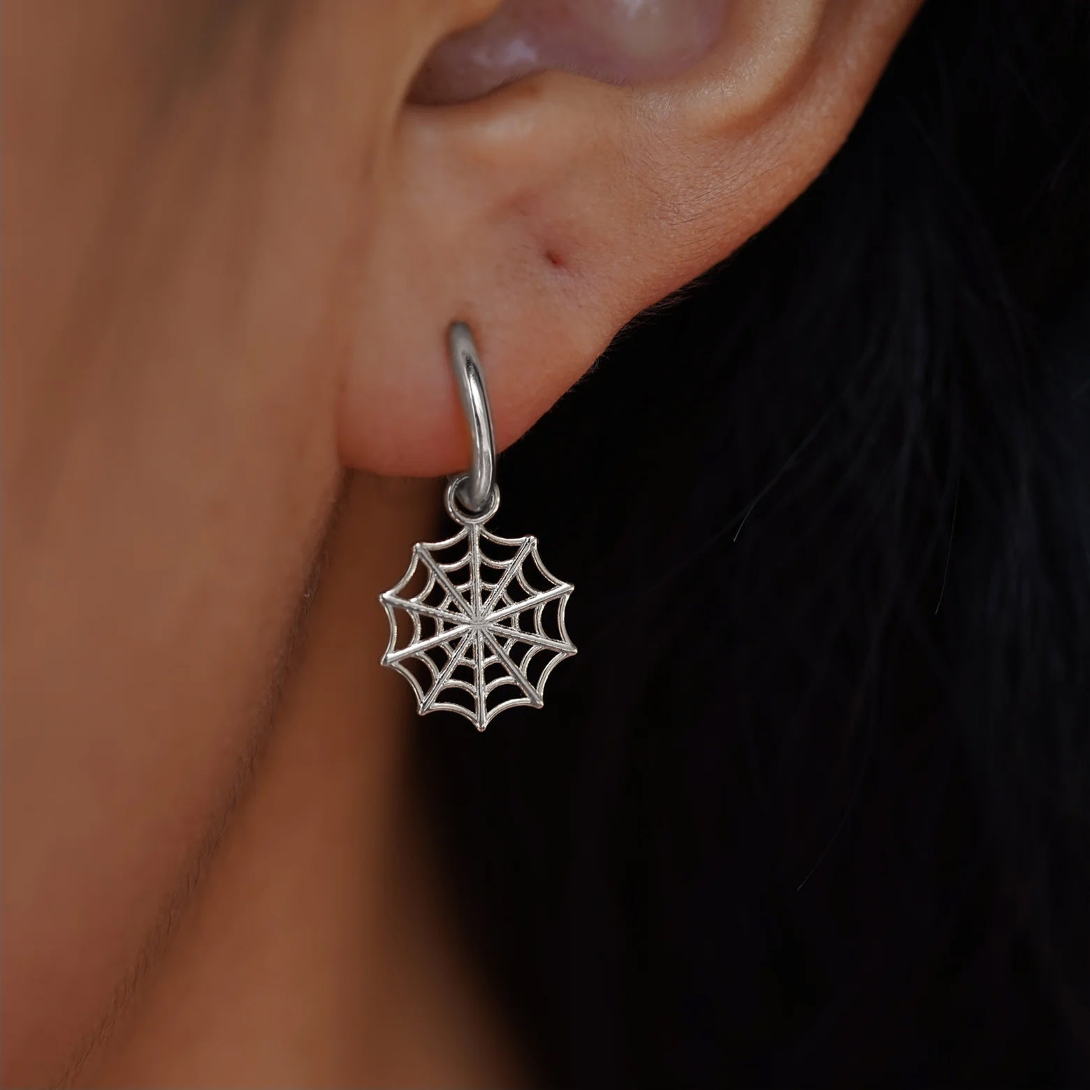 Close up view of a model's ear wearing a white gold Spider Web Charm on a Curvy Huggie Hoop