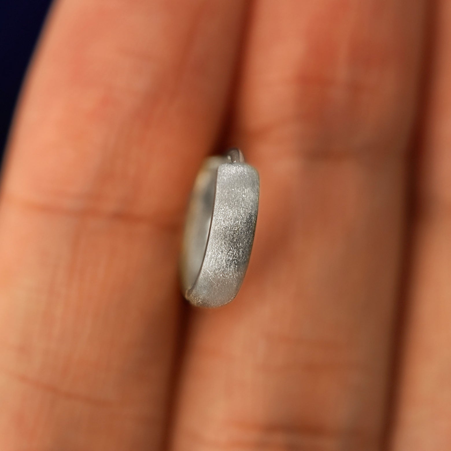 A white gold Stardust Small Thick Huggie Hoop Earring held in between a model's fingers to show the hoops thickness
