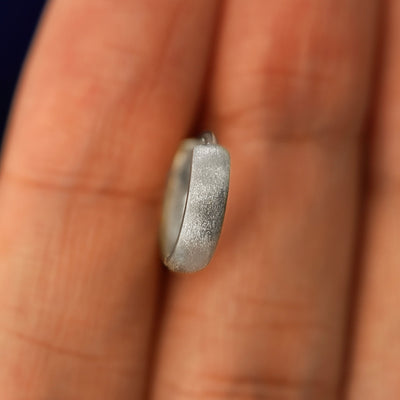 A white gold Stardust Small Thick Huggie Hoop Earring held in between a model's fingers to show the hoops thickness