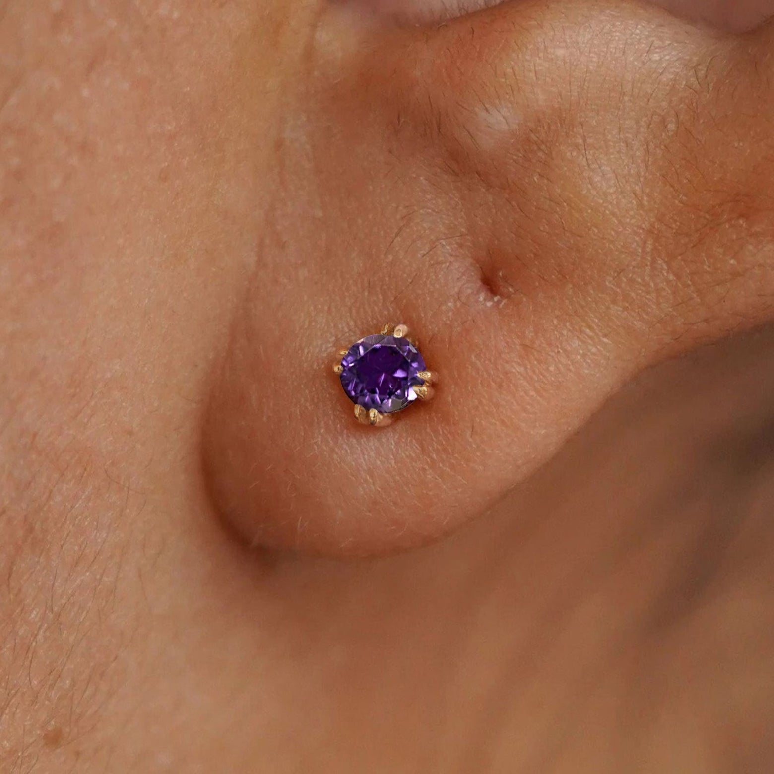 Close up view of a model's ear wearing a 14k yellow gold Amethyst Stud Earring