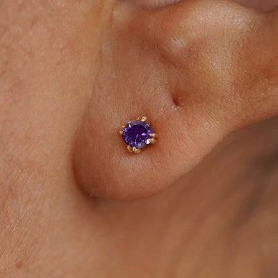 Close up view of a model's ear wearing a 14k yellow gold Amethyst Stud Earring