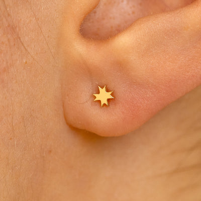 Close up view of a model's ear wearing a yellow gold 8 pointed star earring