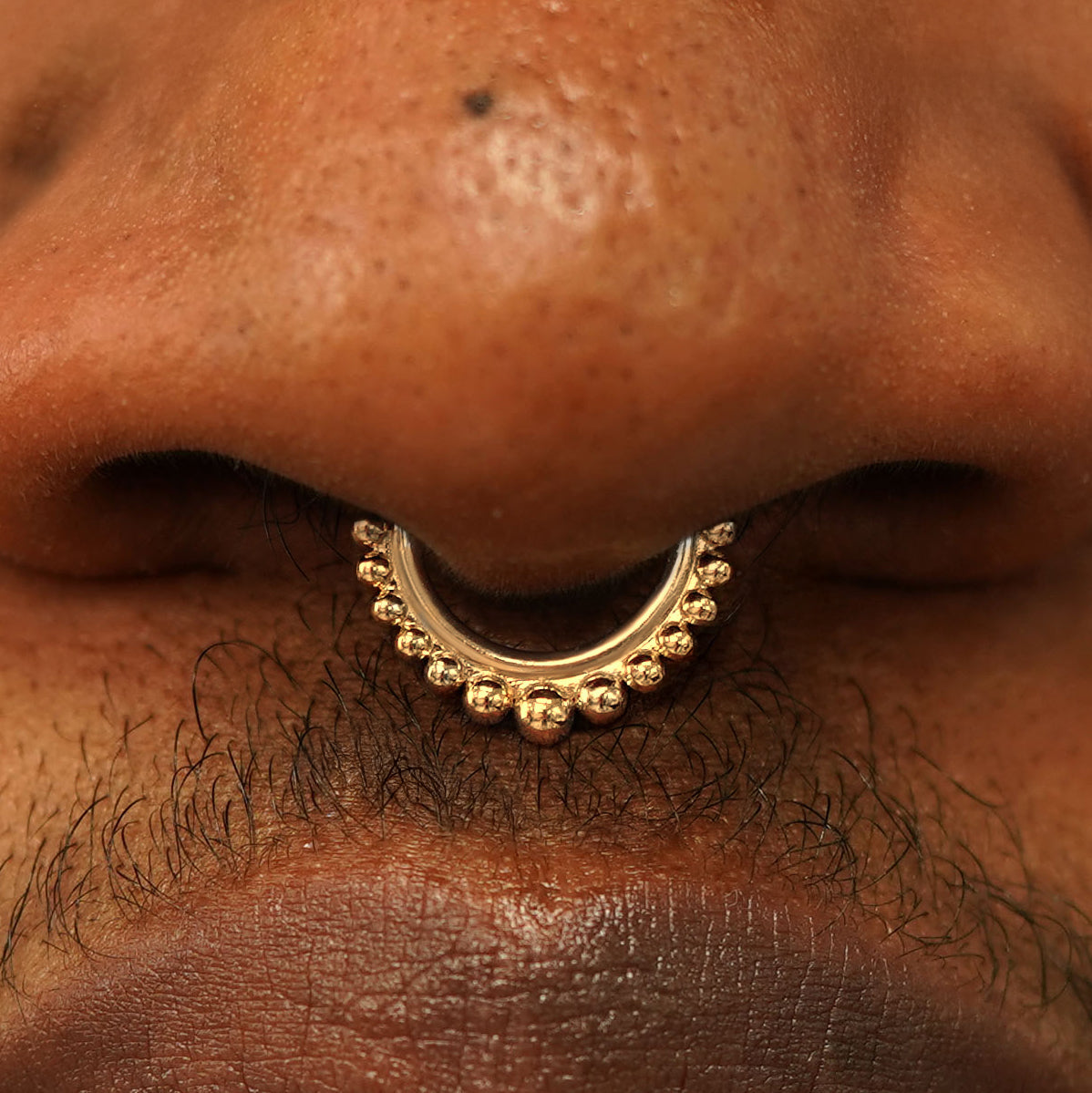 Close up view of a model's nose wearing a 14k yellow gold Beaded Septum