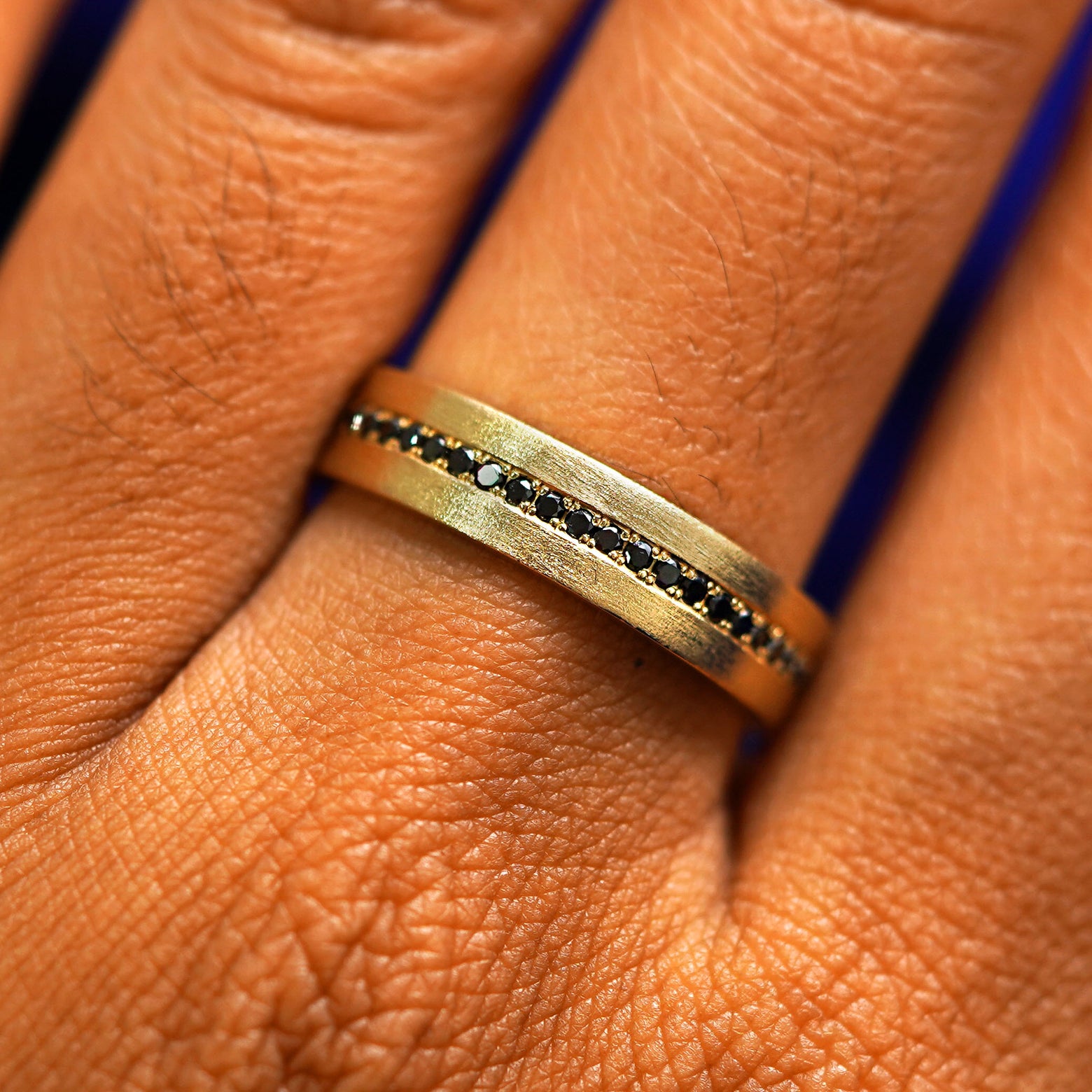 Close up view of a model's fingers wearing a 14k yellow gold Endless Black Diamond Band