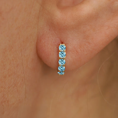 Close up view of a model's ear wearing a yellow gold Mini Light Blue Lab Diamond Huggie Hoop