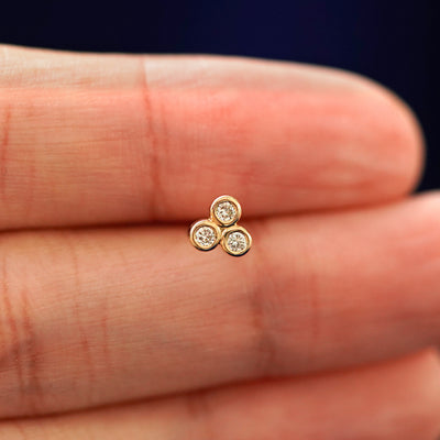 A hand holding a 14k yellow gold Diamond Trio stud earring in between their fingers