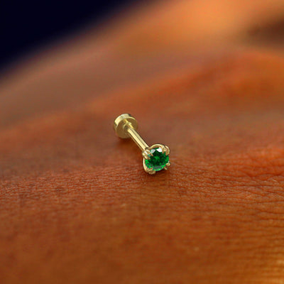 A solid 14k yellow gold emerald Flatback Piercing resting on the back of a model's hand