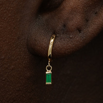 Close up view of a model's ear wearing a yellow gold Baguette Emerald Dangle Huggie Hoop