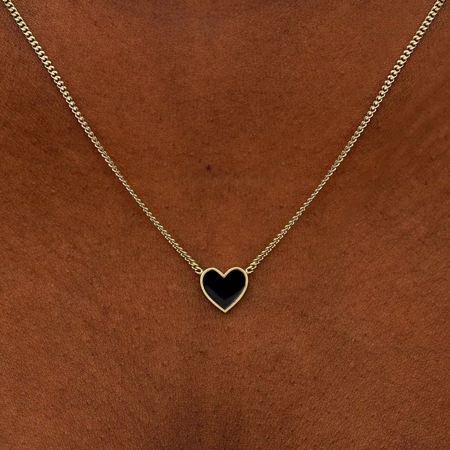 Close up view of a model's neck wearing a yellow gold black enamel heart necklace