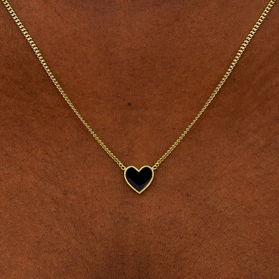 Close up view of a model's neck wearing a yellow gold black enamel heart necklace