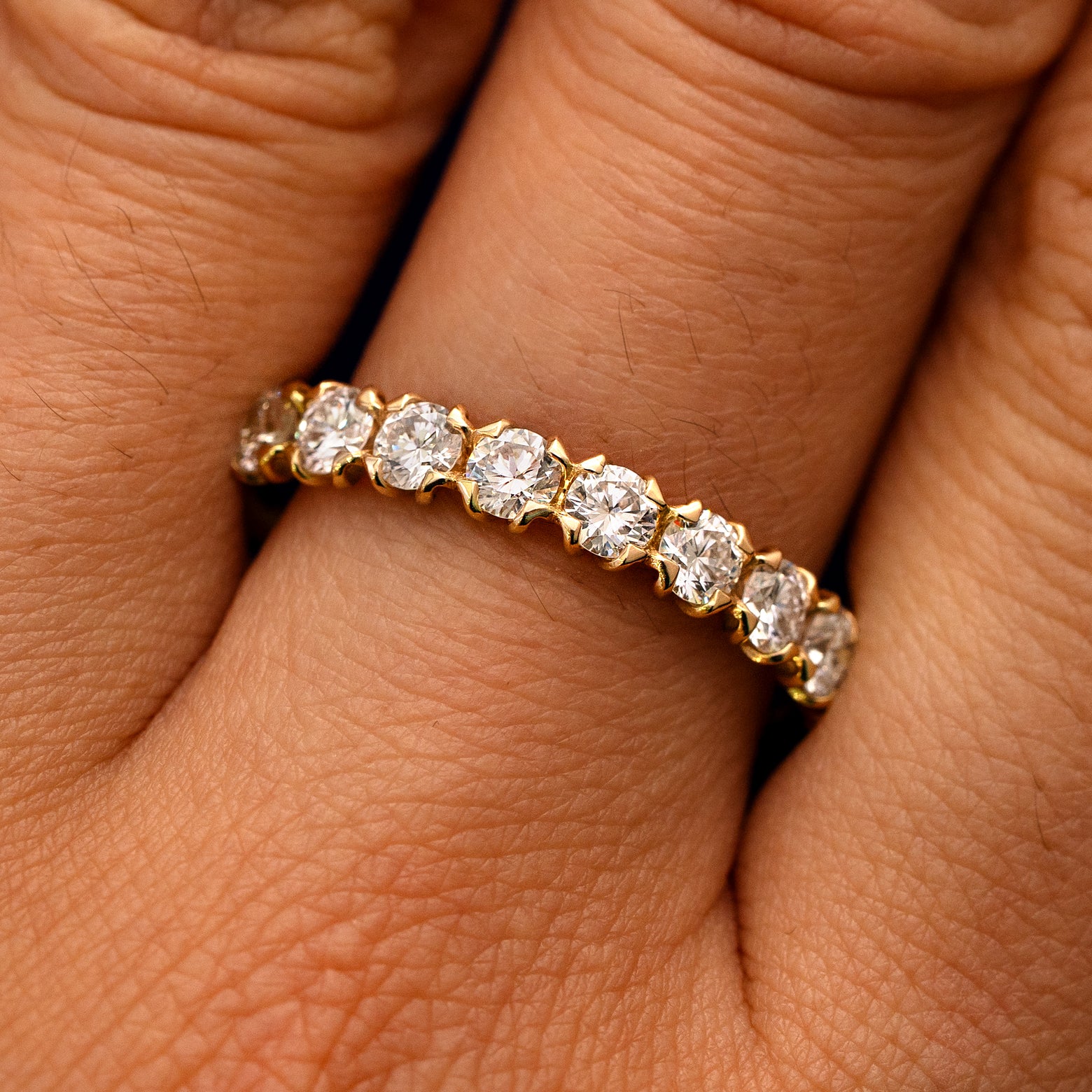 Close up view of a model's fingers wearing a 14k yellow gold Petal Set Diamond Eternity Band