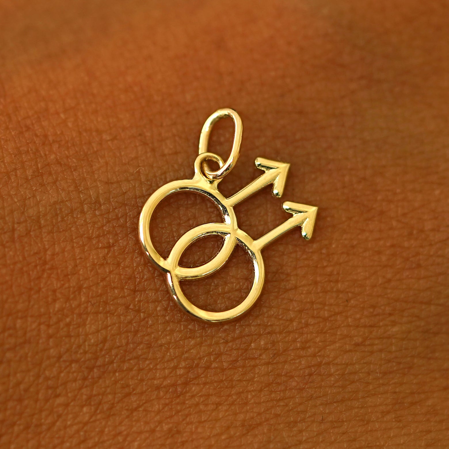 A solid 14k yellow gold Gay Symbol Charm resting on the back of a model's hand