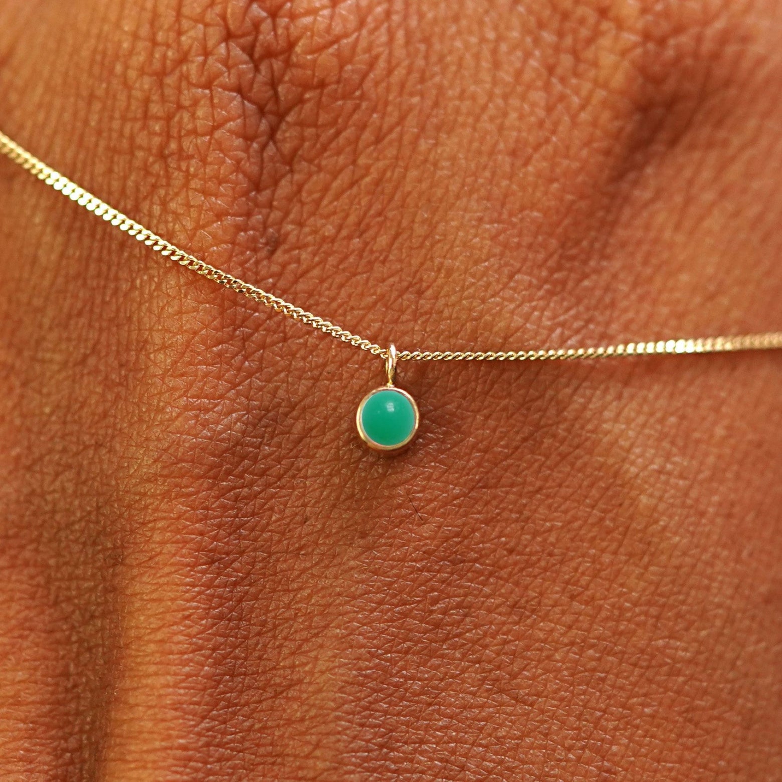 Close up view of a 14k yellow gold Jade Necklace draped across the back of a model's hand