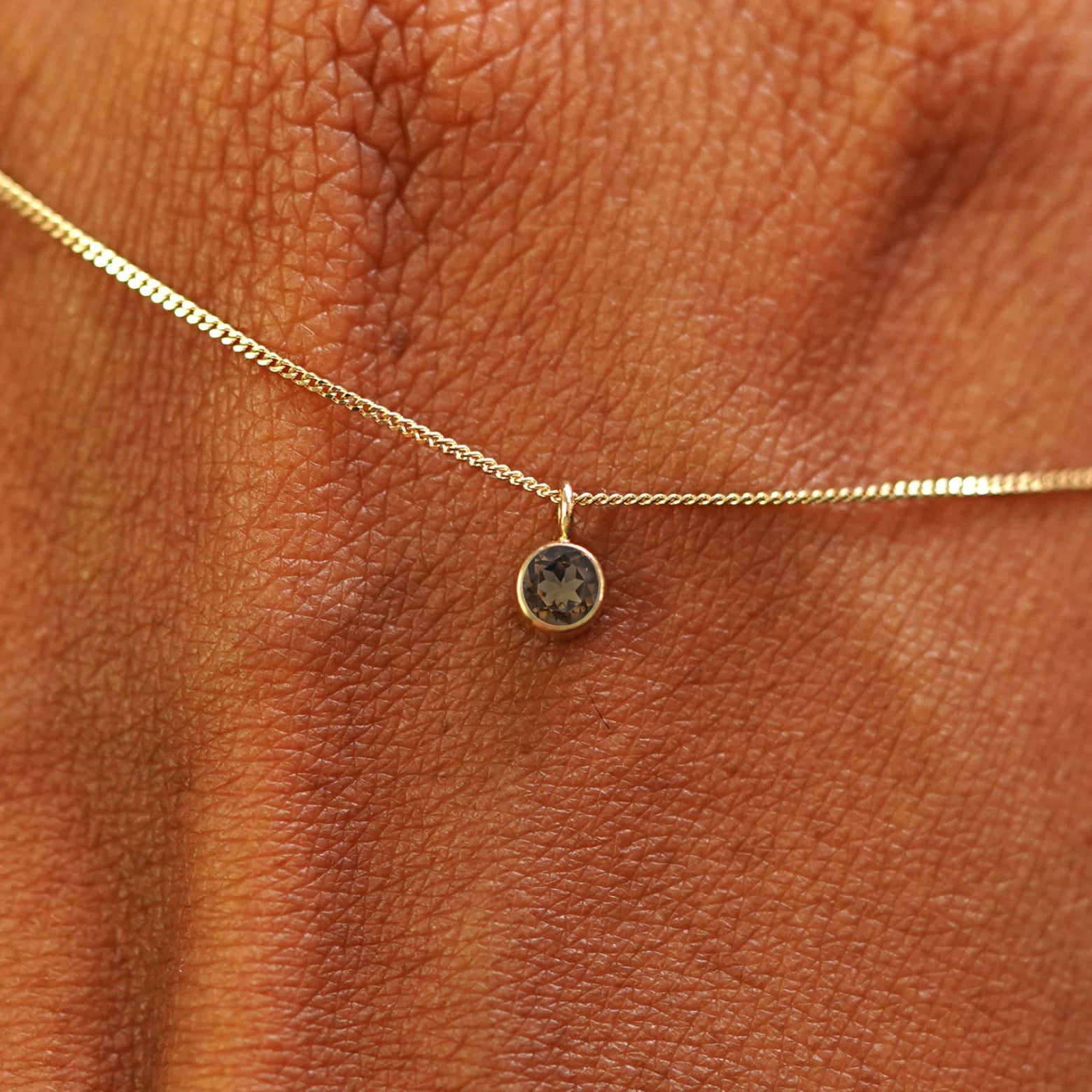 Close up view of a 14k yellow gold Smoky Quartz Necklace draped across the back of a model's hand