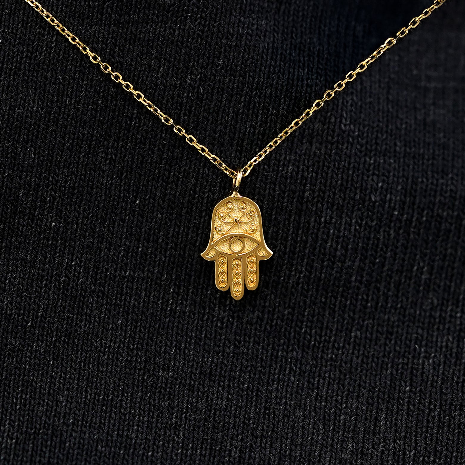 Close up view of a solid 14k yellow gold hamsa necklace against a model's black shirt