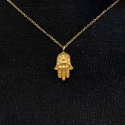 Close up view of a solid 14k yellow gold hamsa necklace against a model's black shirt