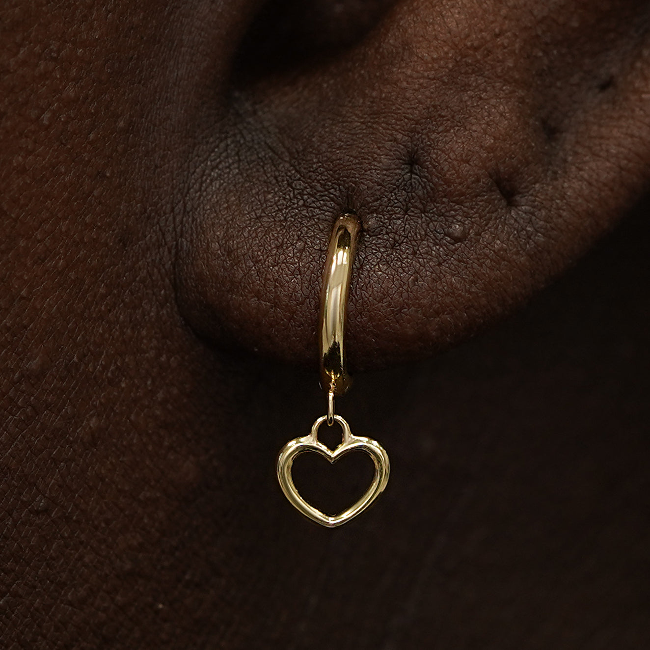 Close up view of a model's ear wearing a yellow gold Heart Dangle Huggie Hoop