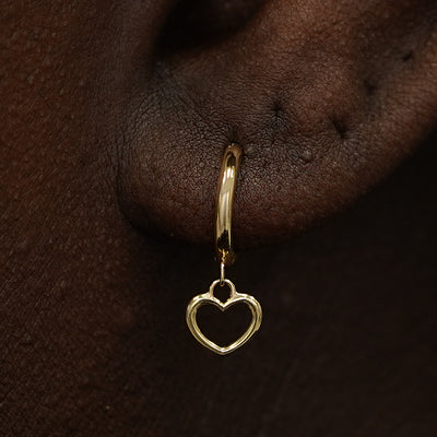 Close up view of a model's ear wearing a yellow gold Heart Dangle Huggie Hoop