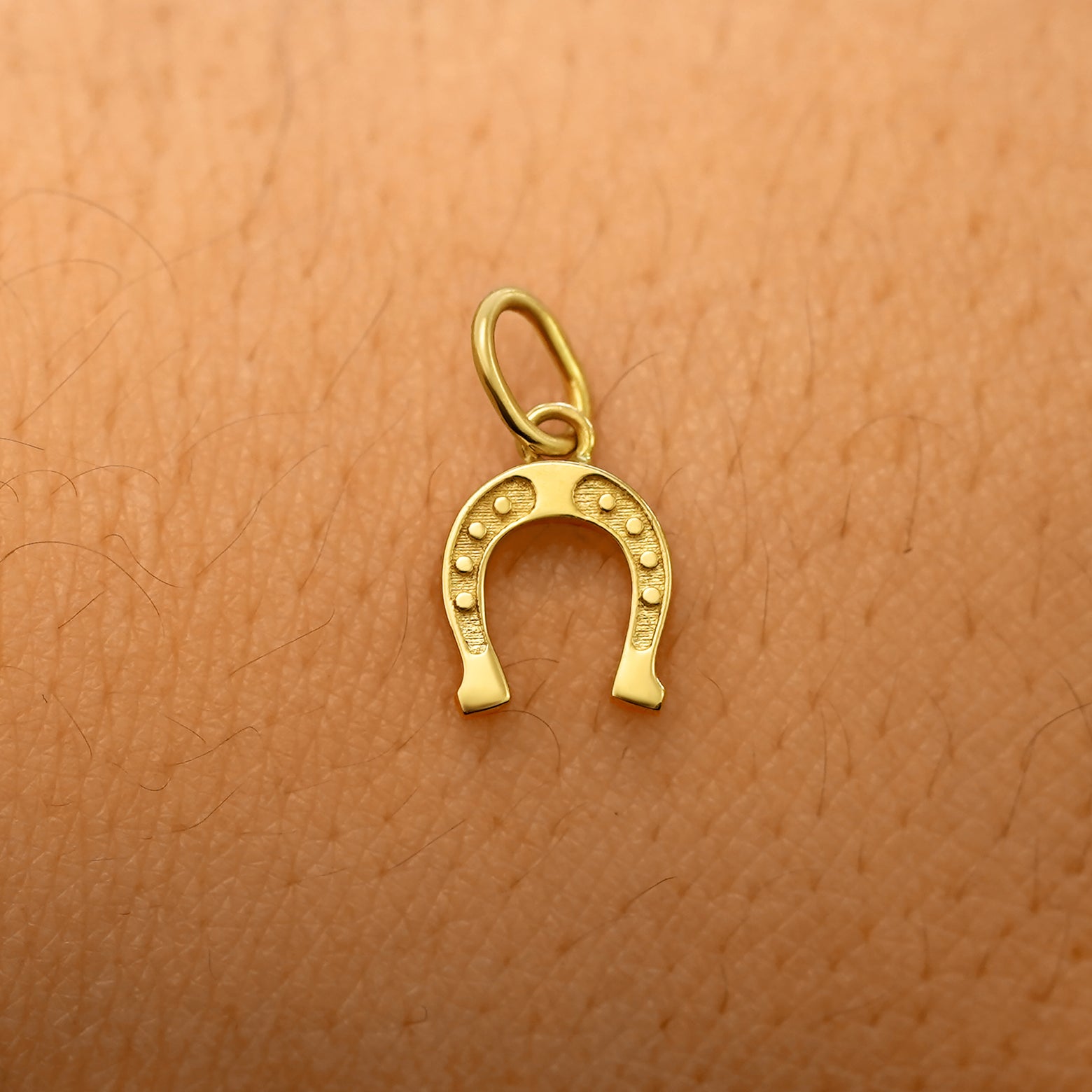 A solid 14k yellow gold Horseshoe Charm resting on the back of a model's hand