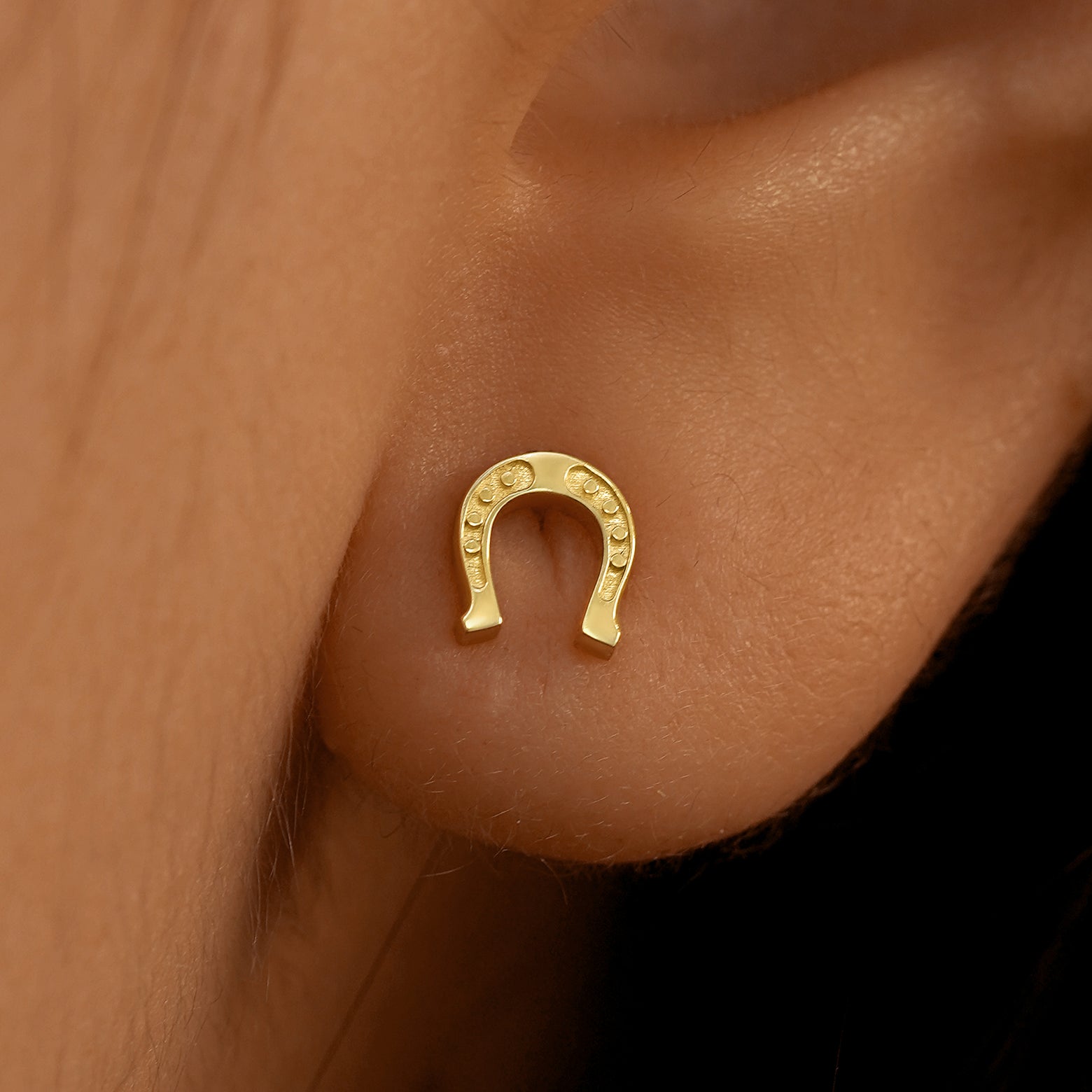 Close up view of a model's ear wearing a 14k yellow gold Horseshoe Earring