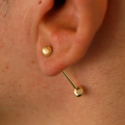 Close up view of a model's ear wearing a 14k yellow gold Large Straight Barbell through a lobe piercing